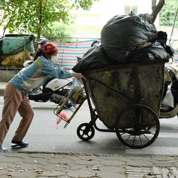 A person pushes an overloaded cart filled with black plastic bags of trash.