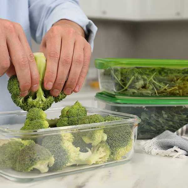 A person putting broccoli into a glass container