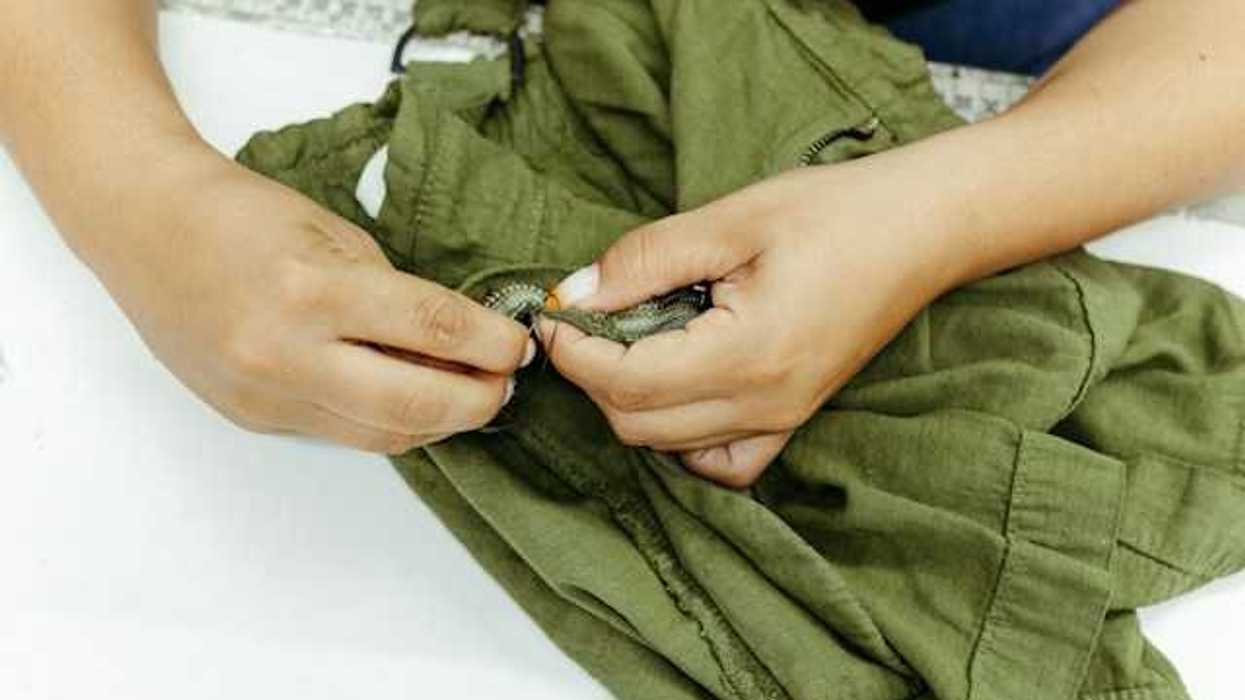 A person repairing a zipper on a pair of green pants