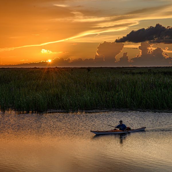 a person rowing a boat on a river at sunset.