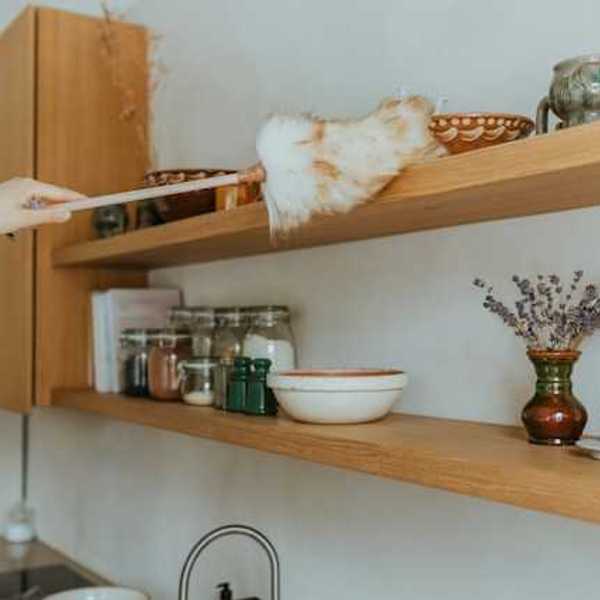 A person running a duster over a tall shelf in a kitchen