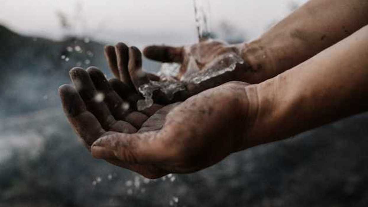 A person's dirty hands with water splashing over them