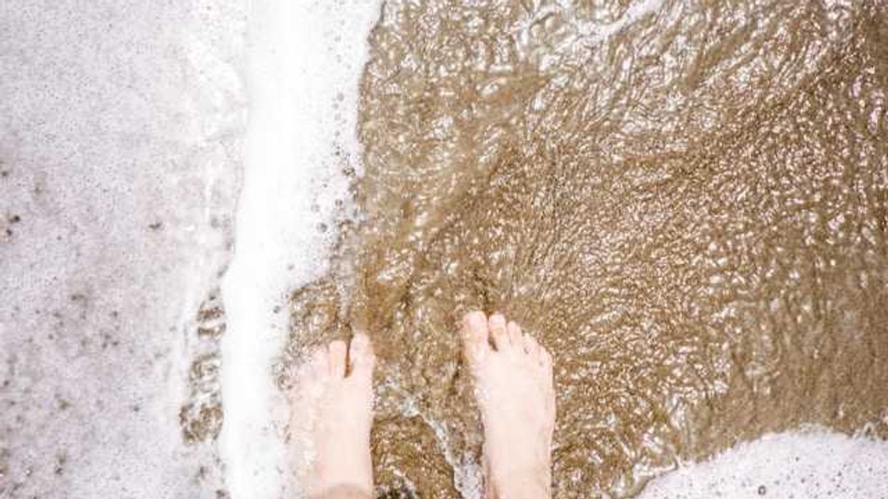 A person's feet on the beach with foamy surf coming in