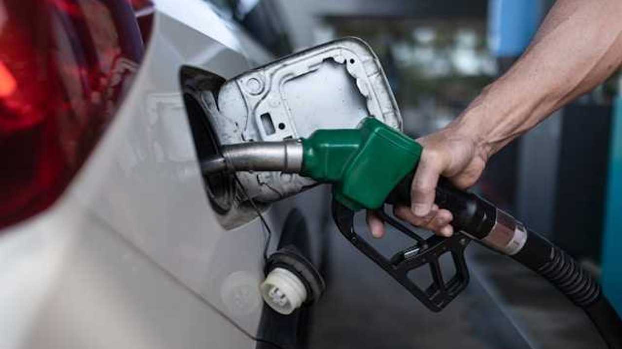A person's hand holding a gas pump while pumping gas into car