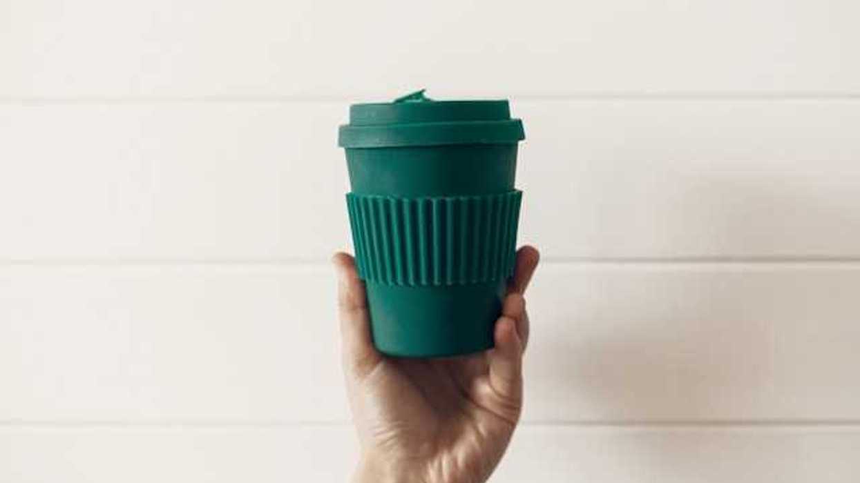 A person's hand holding a green reusable coffee cup