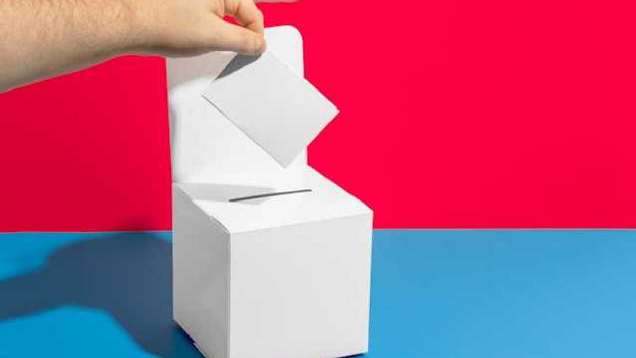 A person's hand placing a piece of paper into a box with a pen in the foreground