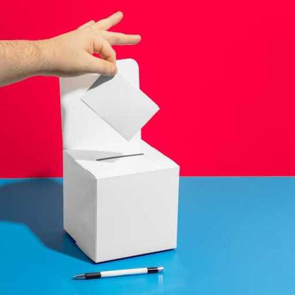 A person's hand placing a piece of paper into a box with a pen in the foreground