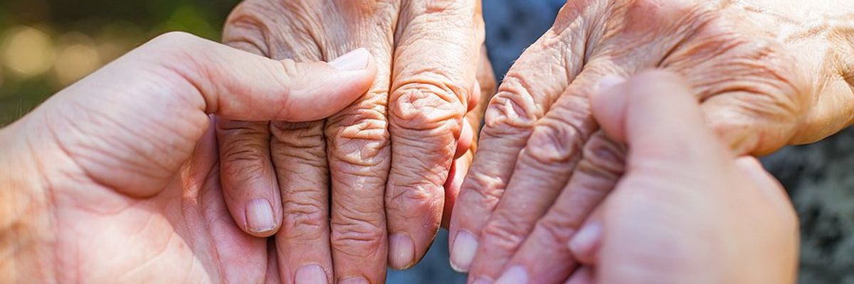 A person's hands holding an elderly woman's hands.