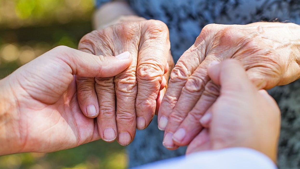 A person's hands holding an elderly woman's hands.