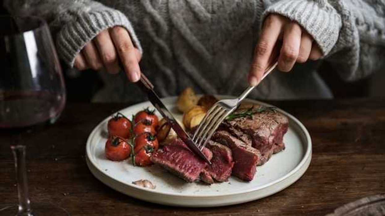A person sitting at a table cutting into a cooked steak on a plate