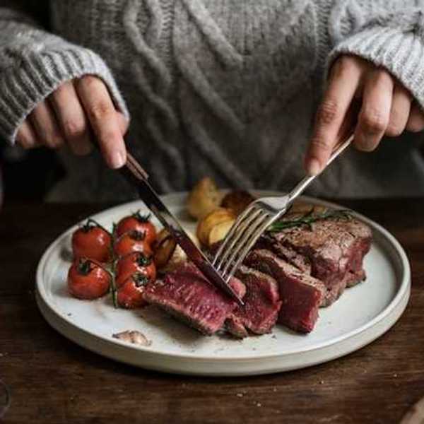 A person sitting at a table cutting into a cooked steak on a plate