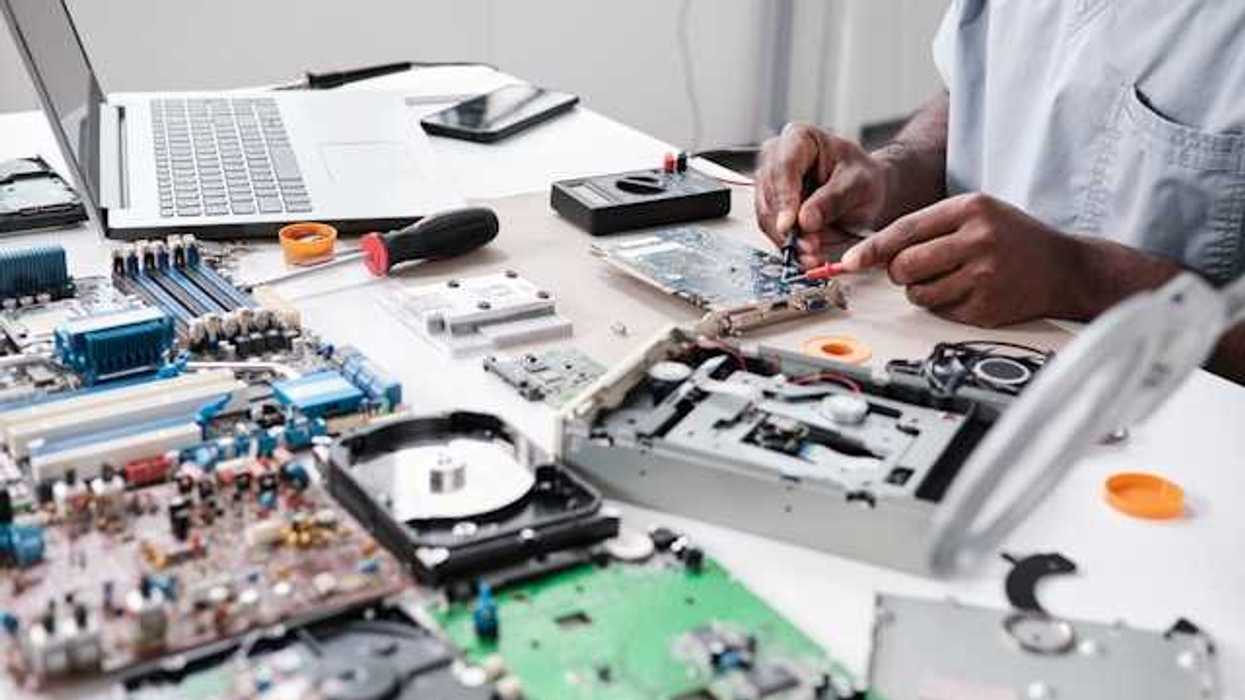A person sitting at a table surrounded by electronic waste such as computer motherboards