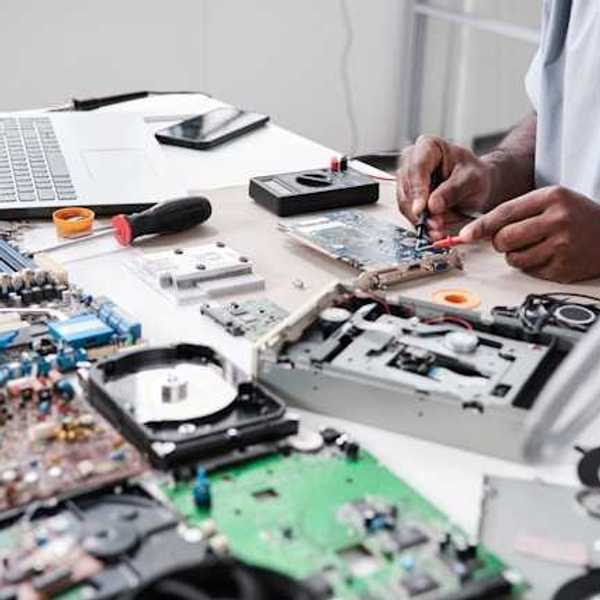 A person sitting at a table surrounded by electronic waste such as computer motherboards