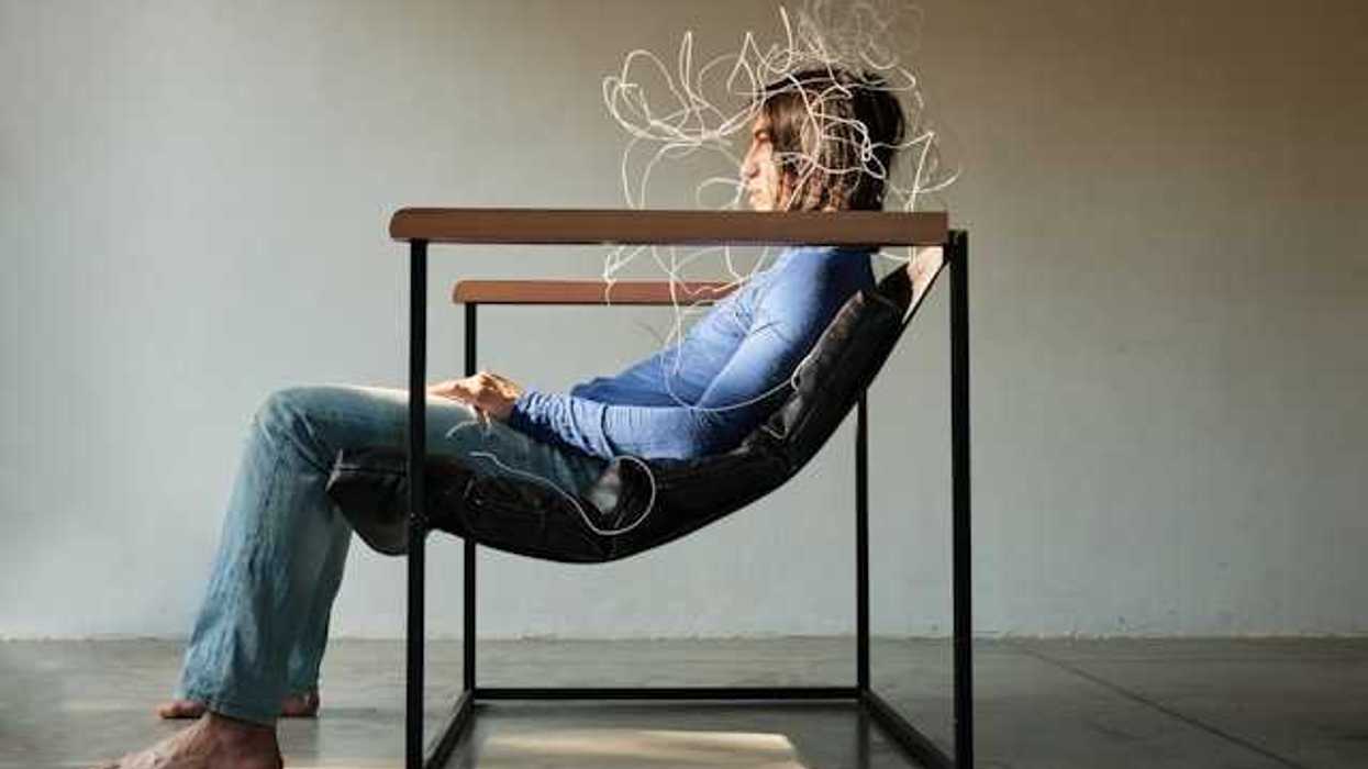 A person sitting in a chair viewed from the side with wires covering their face