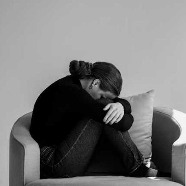 A person sitting in a chair with their head on their knees