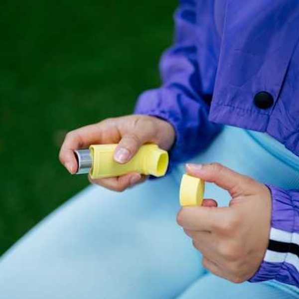 A person sitting in a park with an asthma inhaler in their hands
