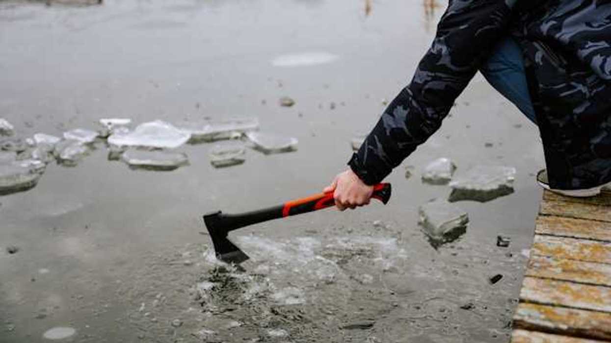 A person sitting on a dock breaking the ice on a lake