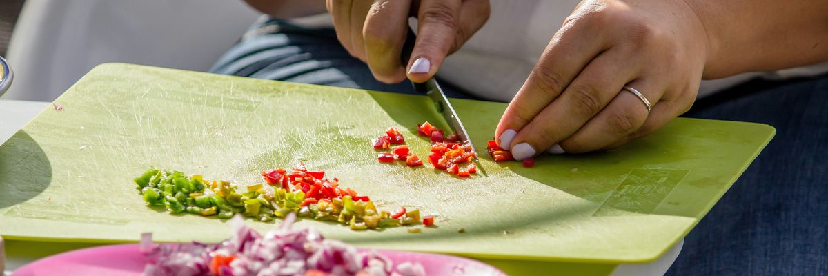 A person slices vegetables on a green plastic cutting board
