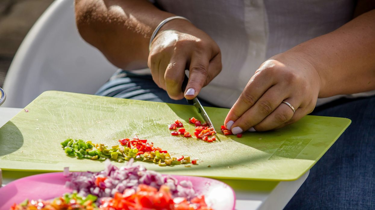 A person slices vegetables on a green plastic cutting board