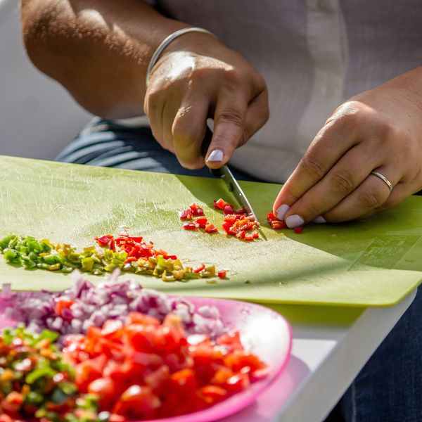 A person slices vegetables on a green plastic cutting board
