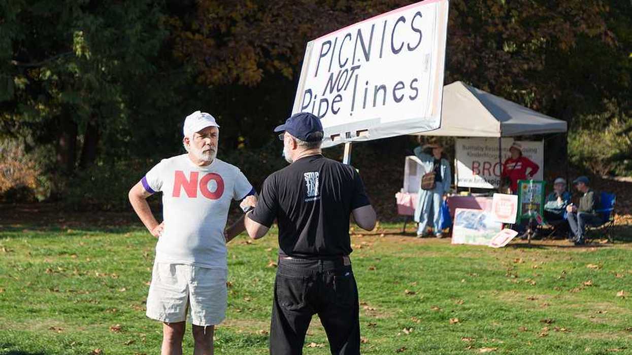 A person standing in a park with a sign saying 'picnics not pipelines'