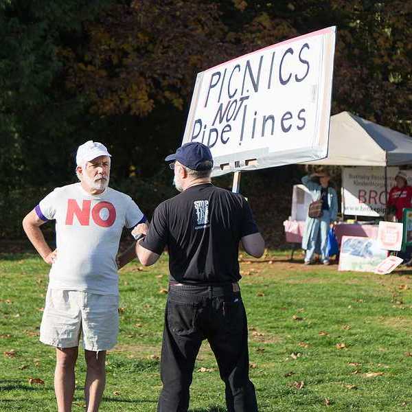 A person standing in a park with a sign saying 'picnics not pipelines'