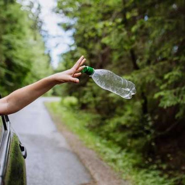 A person throwing a plastic bottle out of a car window