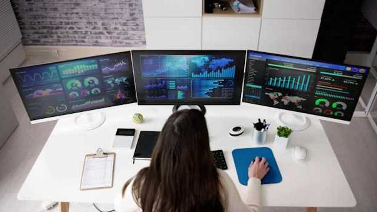 A person viewing three computer monitors with data on them