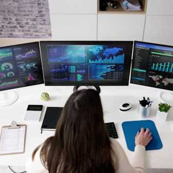 A person viewing three computer monitors with data on them