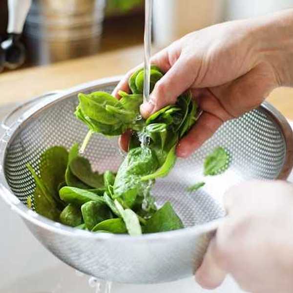 A person washing spinach in a silver colander