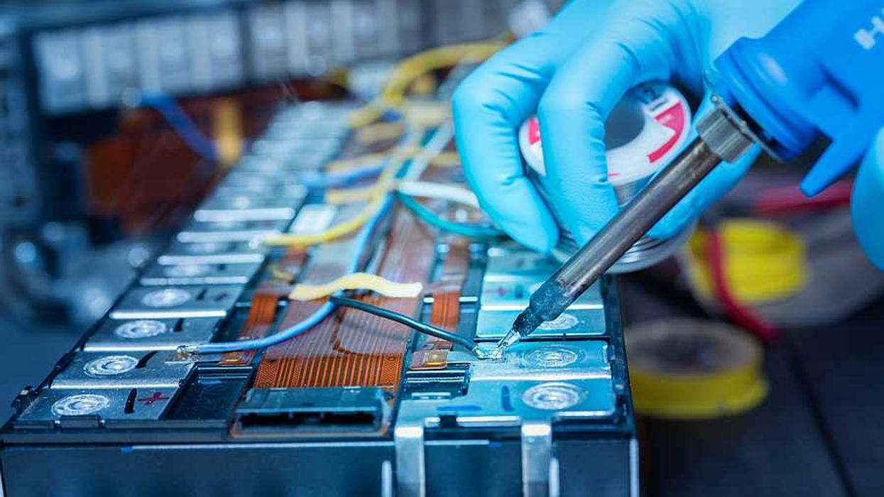 A person wearing blue gloves soldering wire onto a lithium-ion battery