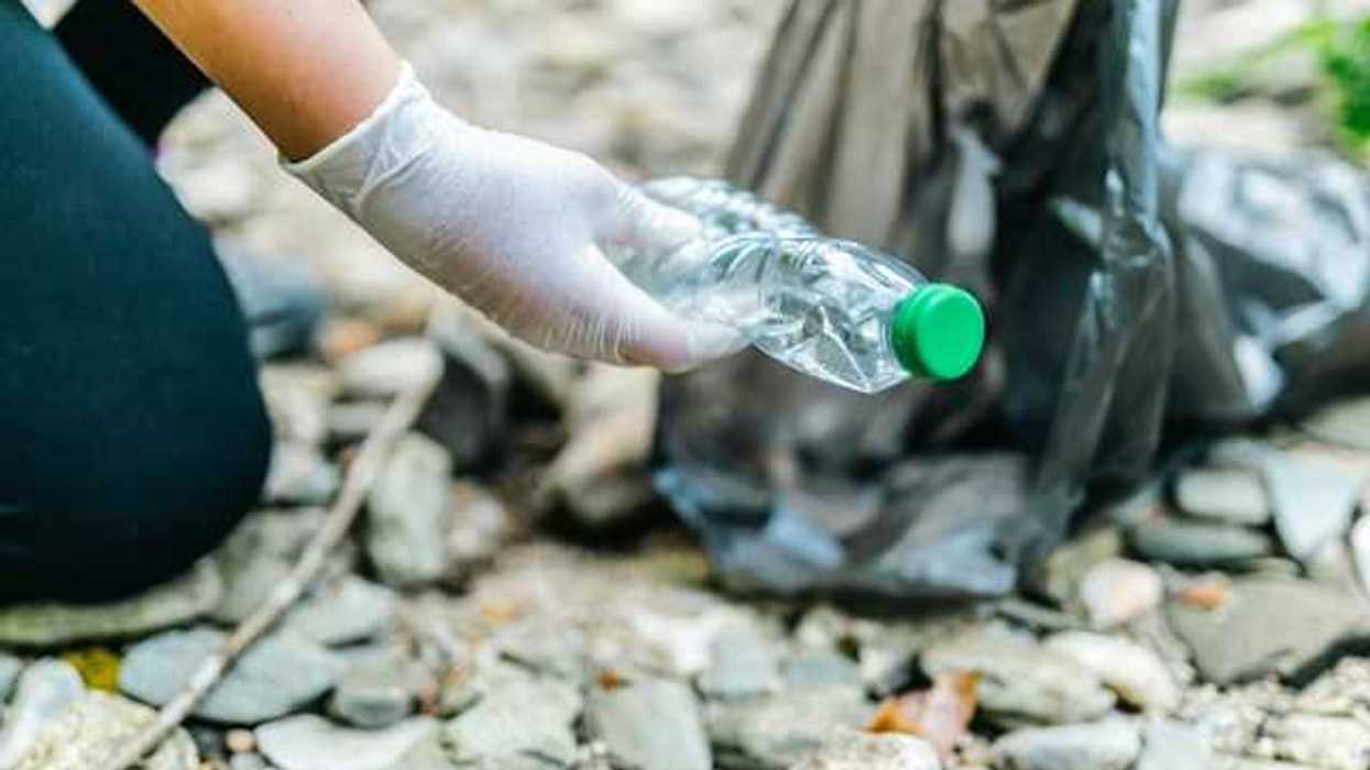 A person wearing gloves putting a plastic bottle into a black plastic bag