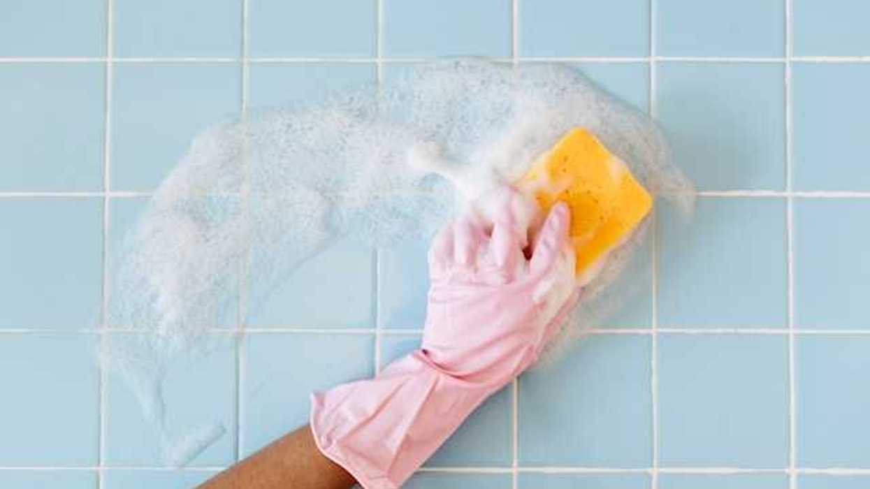 A person wearing pink gloves cleaning a blue tile wall with a sponge