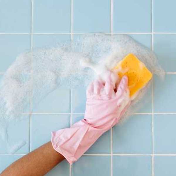 A person wearing pink gloves cleaning a blue tile wall with a sponge