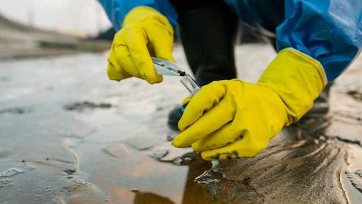 A person wearing yellow gloves collecting a water sample