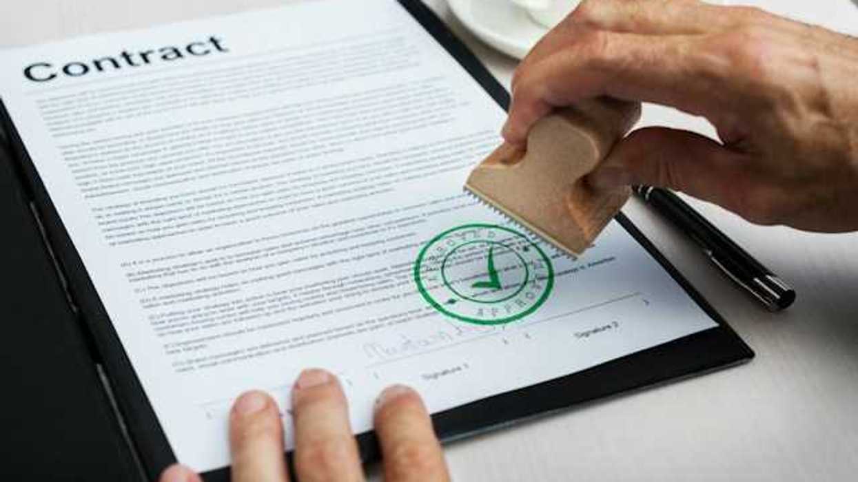 A person with a contract in front of them applying a green 'approved' stamp to the bottom
