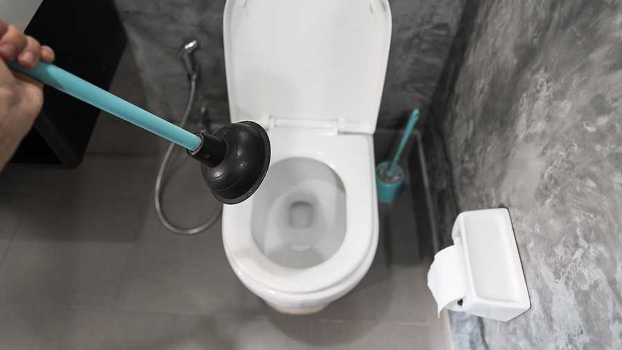 A person with a toilet plunger above a toilet