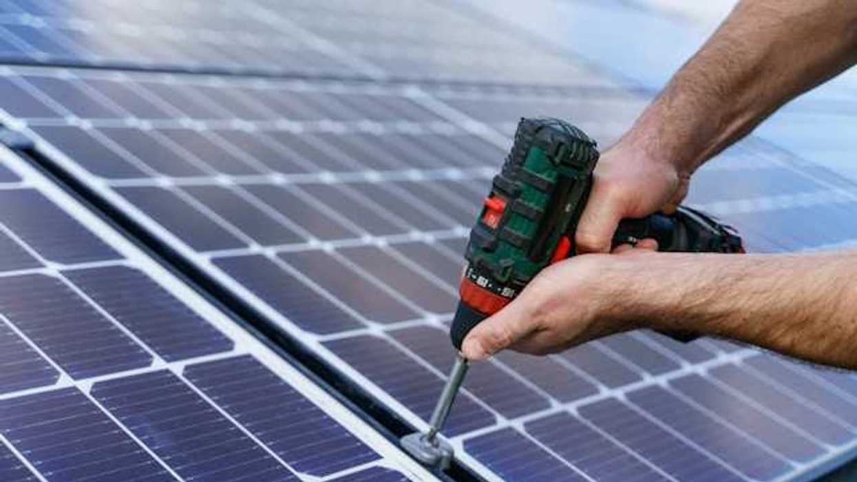 A person with cordless driver installing solar panels