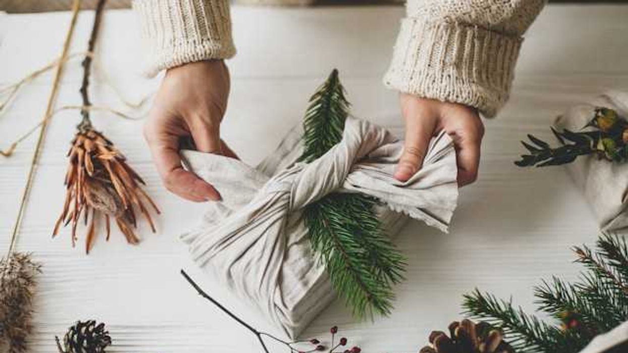 A person wrapping a present with natural fabric, using pinecones and branches as decoration