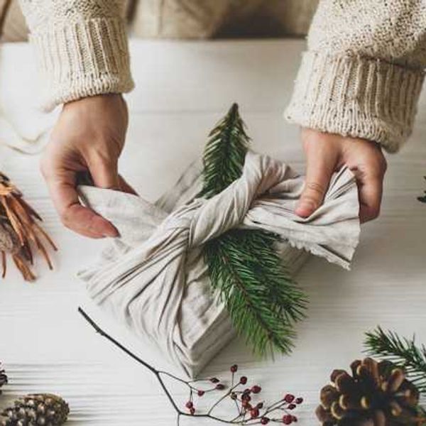 A person wrapping a present with natural fabric, using pinecones and branches as decoration