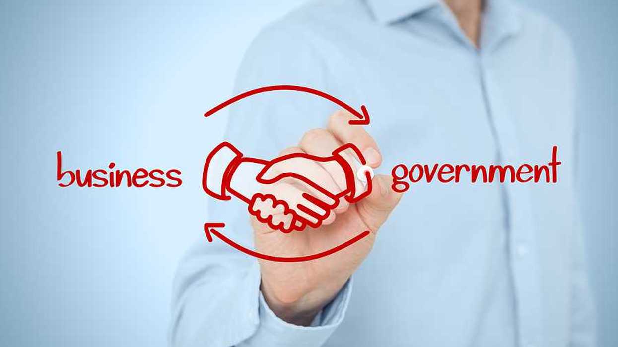 A person writing in red ink the words business and government with clasped hands