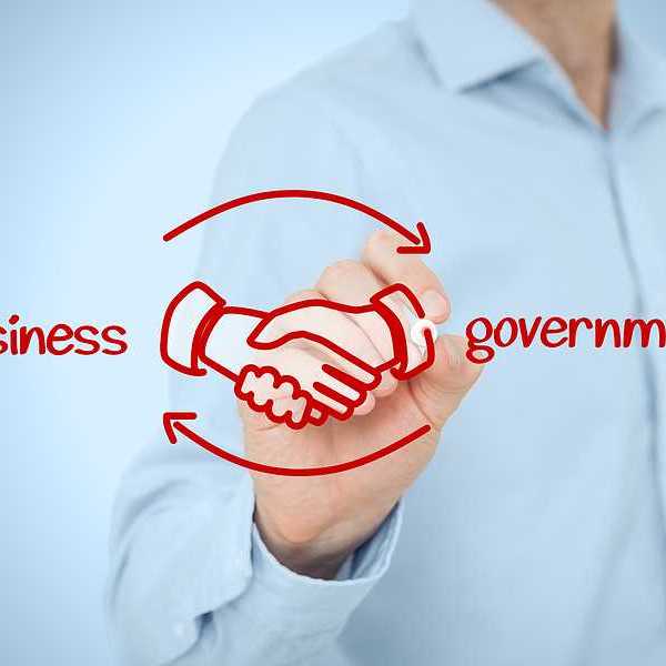 A person writing in red ink the words business and government with clasped hands