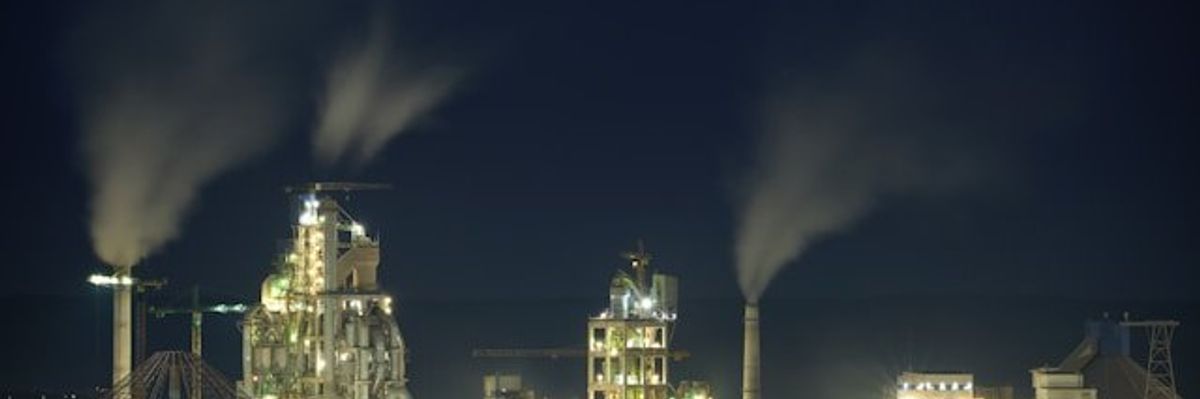 A petrochemical plant lit up at night with smoke billowing from chimneys.