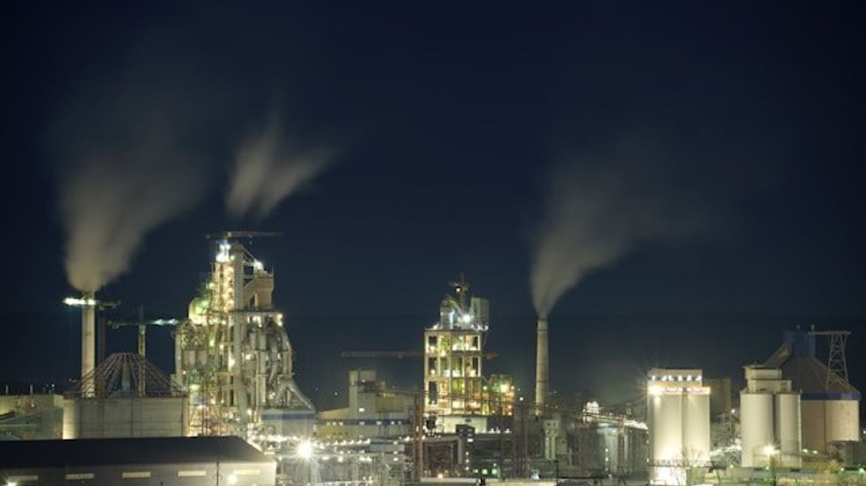 A petrochemical plant lit up at night with smoke billowing from chimneys.