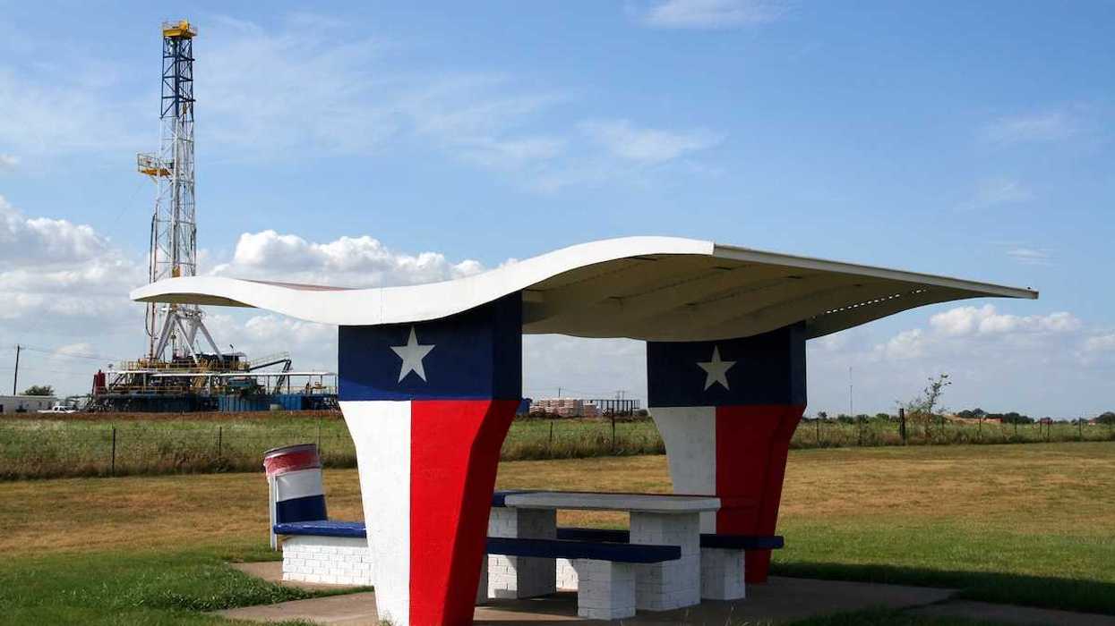 A picnic table at a Texas-motif rest stop with an oil rig in the background.