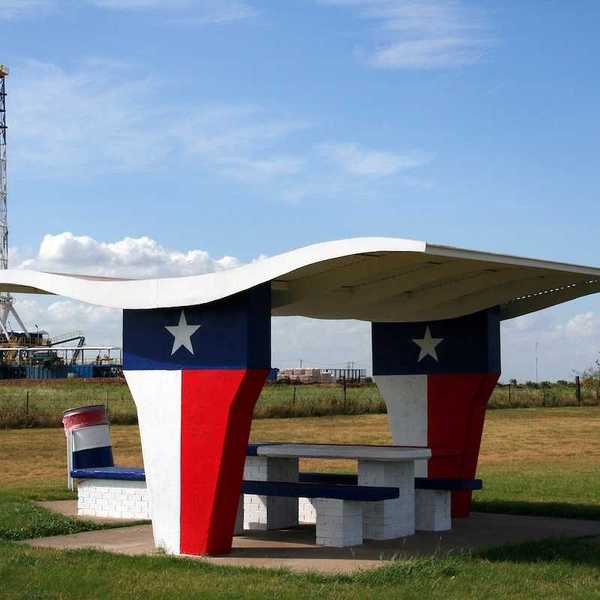 A picnic table at a Texas-motif rest stop with an oil rig in the background.