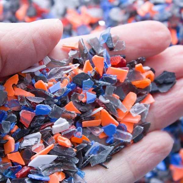 A pile of microplastics - small pieces of hard plastic on palm, intended for further processing.