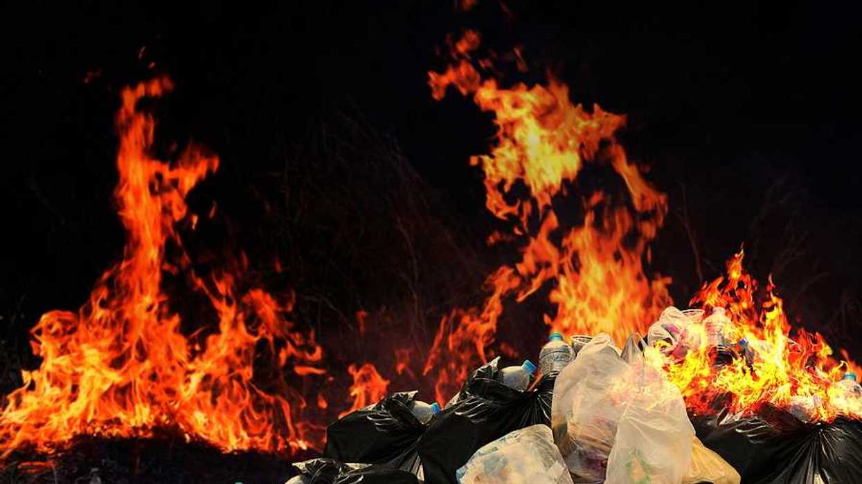 A pile of plastic waste with flames int he background