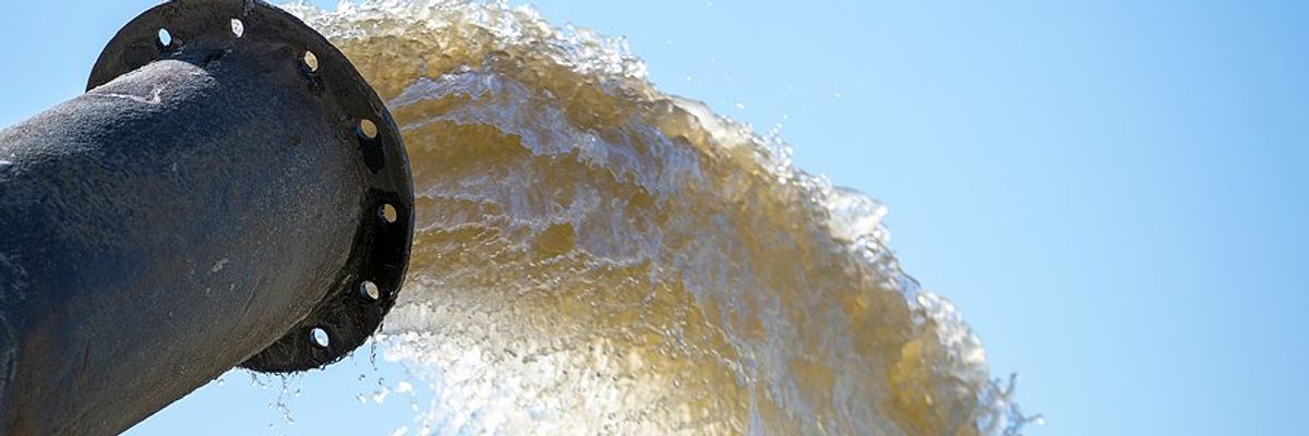 A pipe emitting dirty brown water against a blue sky.
