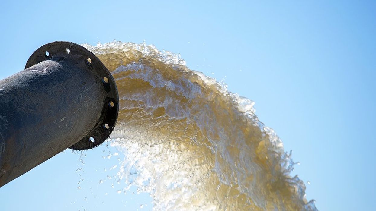 A pipe emitting dirty brown water against a blue sky.
